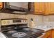 Stove area with black cooktop, wooden cabinets, microwave, neutral tiled backsplash, and granite countertops at 2621 Oldgate Dr # 105, Raleigh, NC 27604