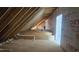 Unfinished attic featuring wood beams, a small window, and insulation at 7934 Wexford Waters Ln, Wake Forest, NC 27587