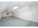 Bright attic space features fresh white paint, blue carpet, and a door, with lighting from a window and overhead fixtures at 1210 Huntsman Dr, Durham, NC 27713