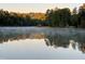 Tranquil lake view with a misty surface, tree-lined shores, and a distant boathouse at 1031 Coldspring Circle, Durham, NC 27705