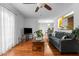 Cozy living room features hardwood floors, ceiling fan, large window with curtains, and gray sofa at 1909 Pearces Rd, Zebulon, NC 27597