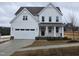 Two-story farmhouse-style home with white siding, a black door, and a two-car garage at 1013 Prominence Dr., Homesite 22, Durham, NC 27712