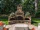 Close-up of an outdoor stone fireplace with a seating area, surrounded by lush landscaping and ambient lighting at 2900 Glenanneve Pl, Raleigh, NC 27608