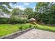 Beautiful backyard featuring a brick patio, lush green lawn, mature trees, and a playhouse with slide at 106 N Trail Dr, Raleigh, NC 27615