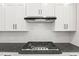 Close-up of a kitchen cooktop with white backsplash, granite countertops, and stainless steel range hood at 9169 Dupree Meadow Dr # 26, Angier, NC 27501