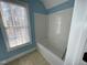 Bright blue bathroom features a white bathtub with tiled surround and natural light from a window with blinds at 1809 Waddill Way, Henderson, NC 27536