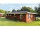 This is a brick home with dark window shutters and mature trees in the yard on a sunny day with a blue sky at 702 Joyner St, Clayton, NC 27520