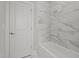 Bathroom showcasing a white bathtub and white marble-look tiled walls, adjacent to a white door and neutral floors at 35 Wheatfield Ln, Youngsville, NC 27596
