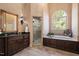 Bright primary bathroom featuring double sinks, a separate glass shower, and a soaking tub beneath an arched window at 2933 Elmfield St, Raleigh, NC 27614
