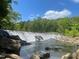Picturesque waterfall cascading over rocks into a calm river surrounded by lush green trees at 1021 Prominence Dr., Homesite 20, Durham, NC 27712