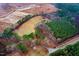 Aerial view shows home nestled within mature trees, with nearby fields and a construction site at 2502 Devils Racetrack Rd, Four Oaks, NC 27524