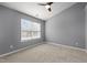 An empty bedroom featuring neutral carpet, grey walls, white trim, ceiling fan and natural light at 1217 Maroon Dr, Durham, NC 27713