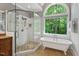 Chic bathroom featuring a glass-enclosed shower, soaking tub, and an arched window with a scenic outdoor view at 216 Copper Beech Ct, Chapel Hill, NC 27517