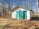 A rundown shed with white paint and blue doors sits on a lot covered in dead leaves at 4051 Silk Hope Gum Springs Rd, Pittsboro, NC 27312