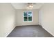 A carpeted bedroom with a single window showing trees outside and a white door on the right side at 5803 Osprey Cove Dr, Raleigh, NC 27604