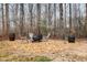 Backyard seating area with a fire pit, gray chairs, wooden barrel tables, and surrounded by trees at 296 Trenburg Pl, Clayton, NC 27520