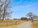 Gravel driveway with fencing on both sides and a large field with a tree line in the distance at 9550 Silk Hope Liberty Rd, Siler City, NC 27344