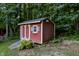 Exterior view of a garden shed with red wood siding, a white door, one window, and surrounded by a lush green forest at 276 Sagamore Dr, Louisburg, NC 27549