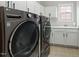 Modern laundry room with front-loading washer and dryer, white cabinets, and tiled floor at 3025 Osterley St, Raleigh, NC 27614