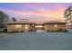 Inviting single-story home featuring a brown exterior, elegant landscaping, and a gravel driveway, set beneath a vibrant sunset sky at 1018 Terrell Woods Ln, Chapel Hill, NC 27516