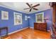 Blue painted bedroom featuring hardwood floors, two windows, and a decorative floor lamp at 114 Evelyn Dr, Knightdale, NC 27545