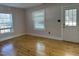 Empty bedroom with hardwood floors, two large windows, and a white door leading to the outside at 4319 Denfield St, Durham, NC 27704