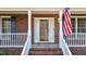 View of a red brick home's front porch and door with white railings, an American flag, and blue shutters at 5317 Chimney Swift Dr, Wake Forest, NC 27587