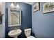 Stylish powder room with blue walls, a pedestal sink, decorative mirror, and framed botanical art at 5520 Advancing Ave, Raleigh, NC 27616
