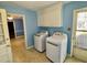 Bright blue laundry room with washer, dryer, overhead cabinet storage, and a view to another blue room at 2118 N Woodland Rd, Henderson, NC 27536
