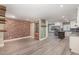 Open living space features brick accent wall, access to the kitchen, and stylish gray wood flooring at 7722 Nc 27 W, Lillington, NC 27546