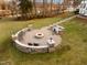 Outdoor circular stone fire pit with seating and a built in grill area in a landscaped yard at 1326 Lochshire Dr, Burlington, NC 27215