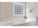 Close up of soaking tub and tile block window in a bright, neutral colored bathroom at 8513 Barrett Hall Ln, Wake Forest, NC 27587