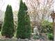 Landscaped backyard with evergreens, flowering trees, a decorative birdhouse, and a charming greenhouse at 401 Lawton Dr, Haw River, NC 27258