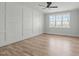 Bright, empty bedroom features a decorative panel wall, hardwood floors, a ceiling fan, and a large window at 100 Sire Ct, Holly Springs, NC 27540