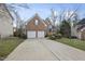Brick house with a two-car garage and a large driveway, surrounded by mature trees, with a yard on a hill at 8720 Deerland Grove Dr, Raleigh, NC 27615
