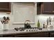 Close-up view of the kitchen cooktop and countertops with stainless vent hood and white subway tile backsplash at 1608 Doubles Ct, Raleigh, NC 27609