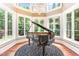 Elegant music room with a grand piano, hardwood floors, and walls of windows at 1801 Oatlands Ct, Wake Forest, NC 27587