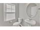 Elegant powder room featuring a pedestal sink, round mirror, and natural light from the window at 1723 Starlit Sky Ln, Cary, NC 27519