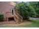 View of a wooden deck and steps attached to the brick house, surrounded by lush greenery at 1017 Holly Creek Ln, Chapel Hill, NC 27516