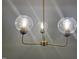 Close up of modern chandelier with three glass globe lights and gold finish at 7780 Brookdale Dr, Raleigh, NC 27616