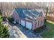 Aerial view of a brick home featuring a two-car garage and spacious driveway surrounded by lush trees at 2030 Lonesome Dove Dr, Franklinton, NC 27525