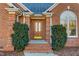 Inviting front entrance with a beautiful wooden door, red brick, trimmed shrubs and brick steps at 2318 Rogers Rd, Graham, NC 27253