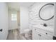 Modern bathroom features a decorative wood wall, round mirror, white vanity, and walk-in shower at 7414 Virgilina Rd, Roxboro, NC 27574