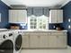 Well-lit laundry room featuring white cabinets, stainless steel appliances, blue walls and a patterned window valance at 107 Marseille Pl, Cary, NC 27511