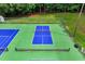 Aerial view shows the bright blue and green tennis court surrounded by a tall fence and mature trees at 632 Angus Ct, Sanford, NC 27332