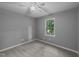 A gray bedroom has a ceiling fan and a window to a leafy yard, neutral carpet and baseboards at 2301 Pastille Ln, Raleigh, NC 27612