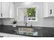 A modern sink with black countertop, white backsplash and cabinet, and window view to the exterior at 905 N Hyde Park Ave, Durham, NC 27701