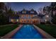 A shot of the house's back exterior, showcasing the pool and well-lit windows at dusk at 109 Chimeneas Pl, Chapel Hill, NC 27517
