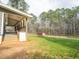 Large backyard with a covered porch, green lawn, mature trees, and a red storage shed at 3130 State Hwy 58, Louisburg, NC 27549