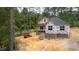New construction home with brick foundation, black roof, and protective wrap against wooded backdrop at 15 Bourbon St, Fuquay Varina, NC 27526